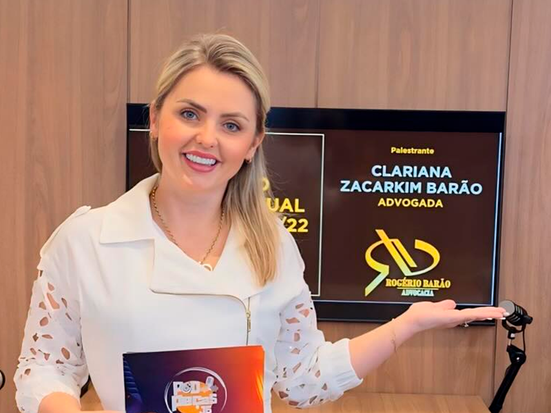 Clariana Barão palestrando em um palco com o banner 'Clariana Zacarkim Barão, advogada'
